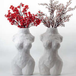 Two white, ceramic vases shaped like women's torsos. The vase on the left has a glossy finish and is holding red flowers in it, while the vase on the right has a matte finish and is holding white flowers.