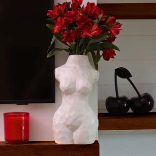 A decorative matte white vase in the shape of a female body displaying red flowers on a floating shelf.