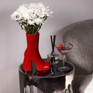 A red boot vase filled with white flowers sits on a table next to a martini glass on a table. 